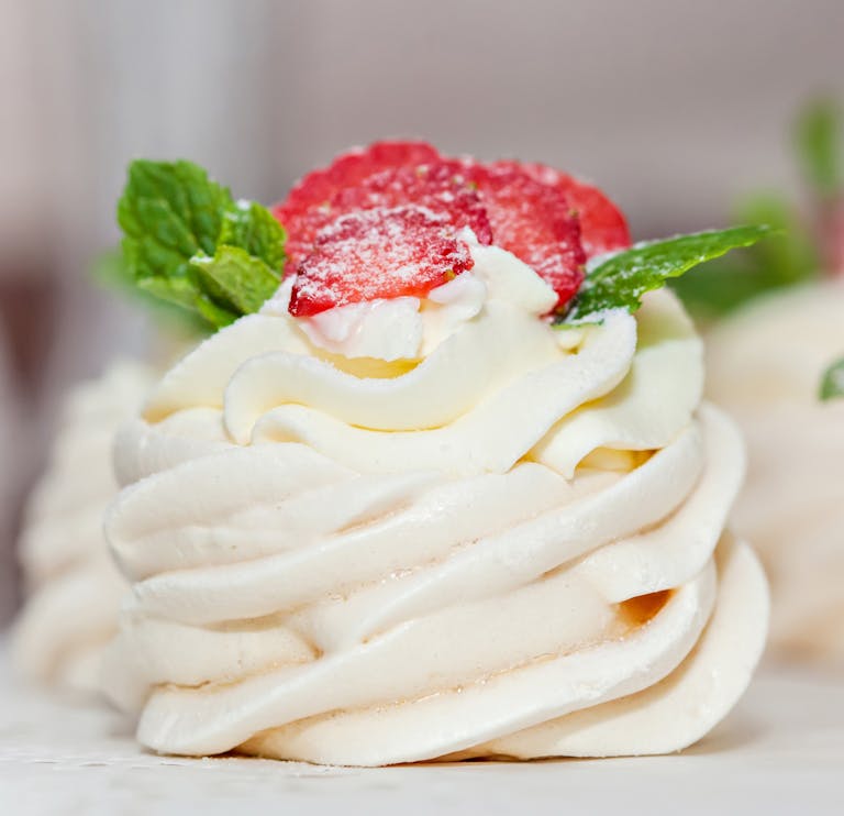 Close-up of a creamy meringue dessert topped with strawberries and mint.