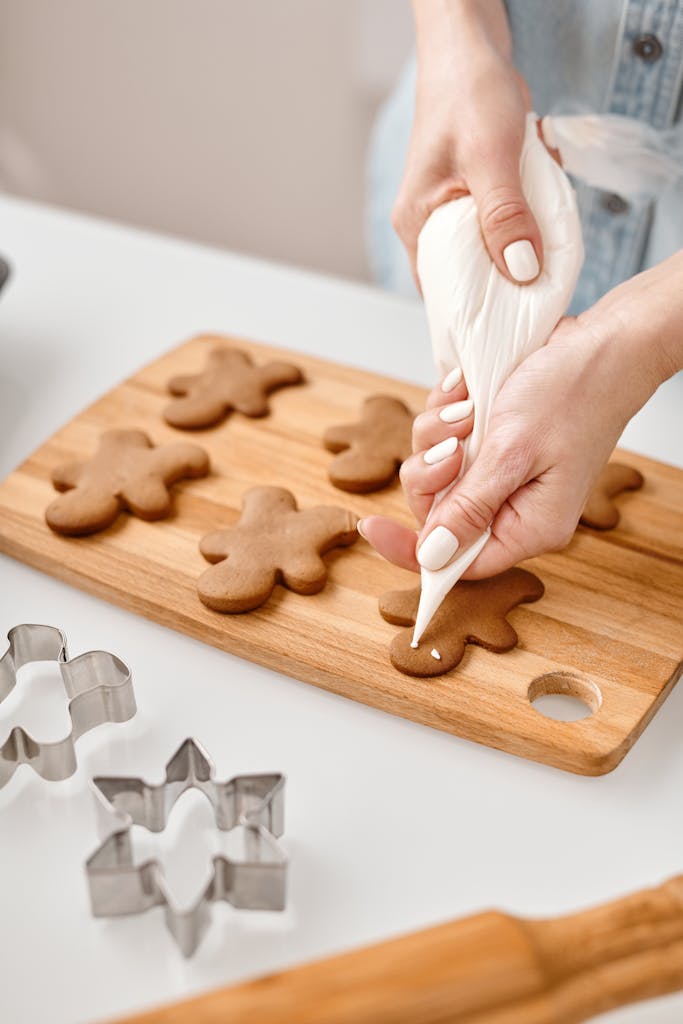 Hands decorating gingerbread cookies with icing, capturing festive preparation.