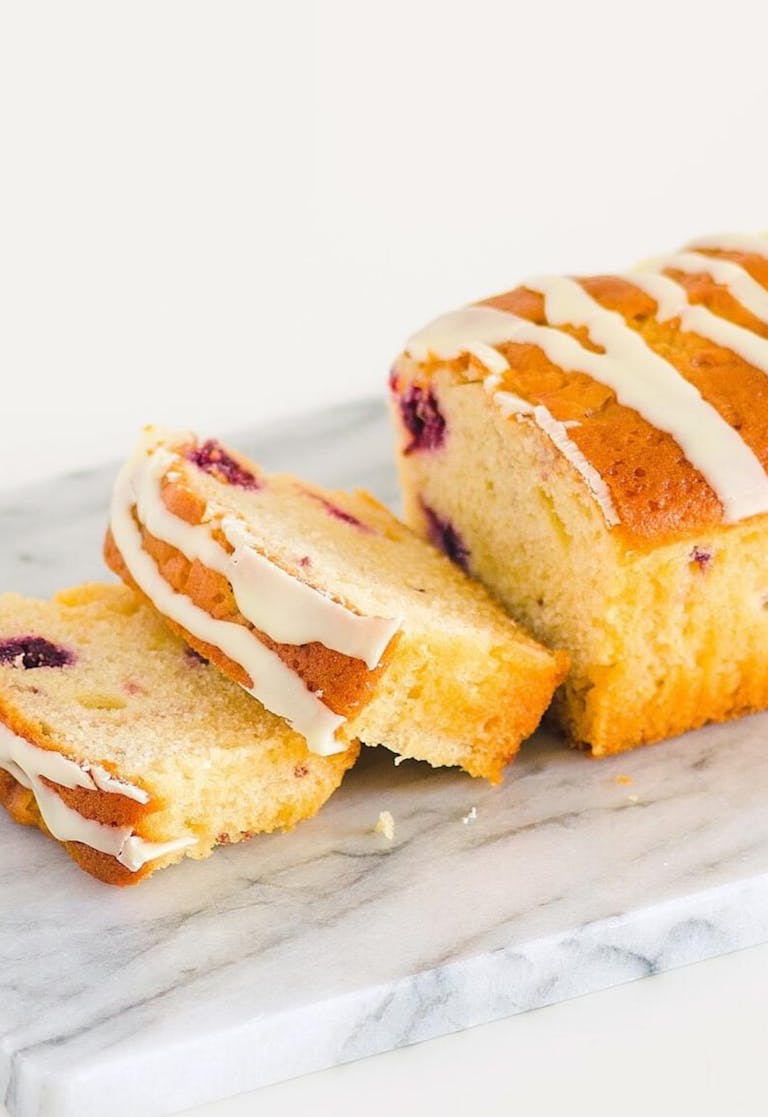 Sliced blueberry pound cake with icing on a marble board, perfect for dessert lovers.