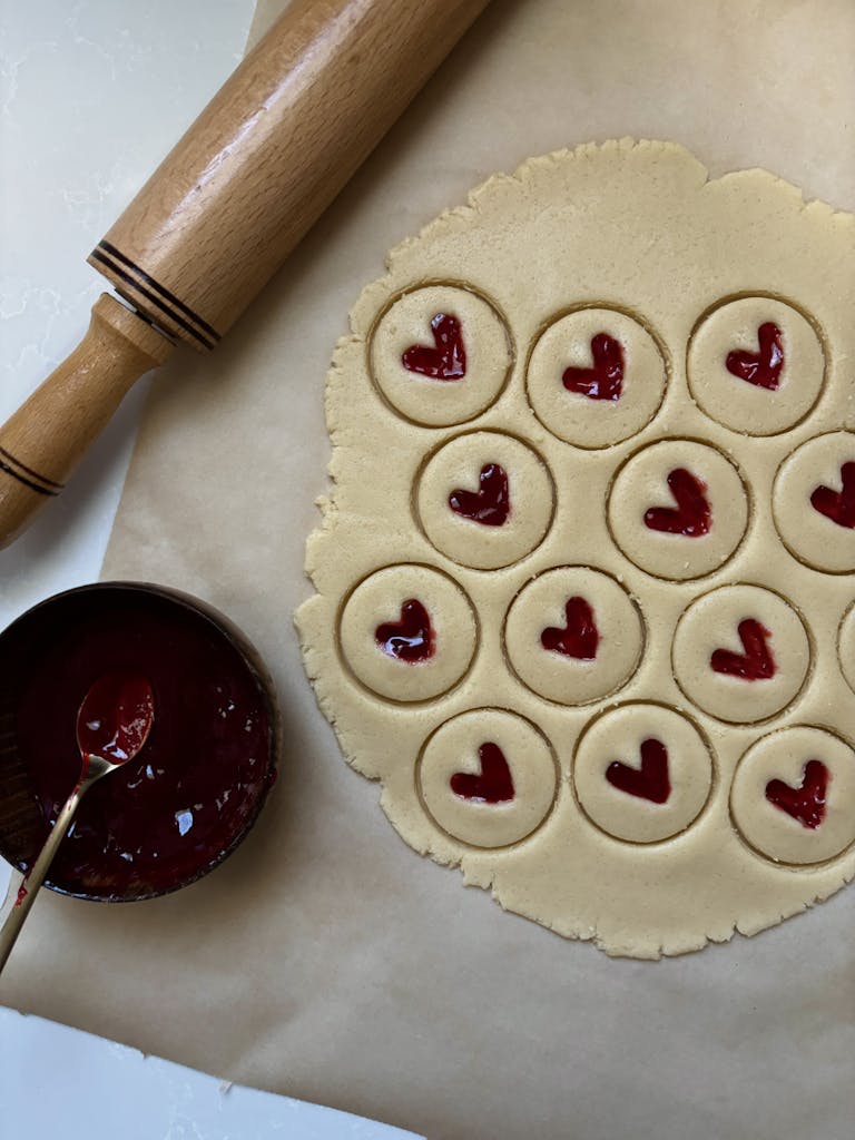 Heart-shaped cookies with jam being prepared on parchment paper.