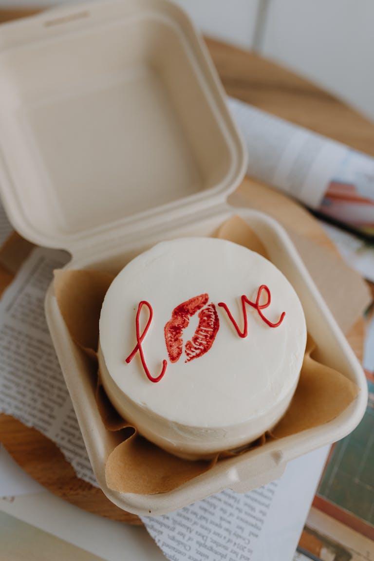 Top view of a white cake with love inscription in an open takeaway box, exuding romance.