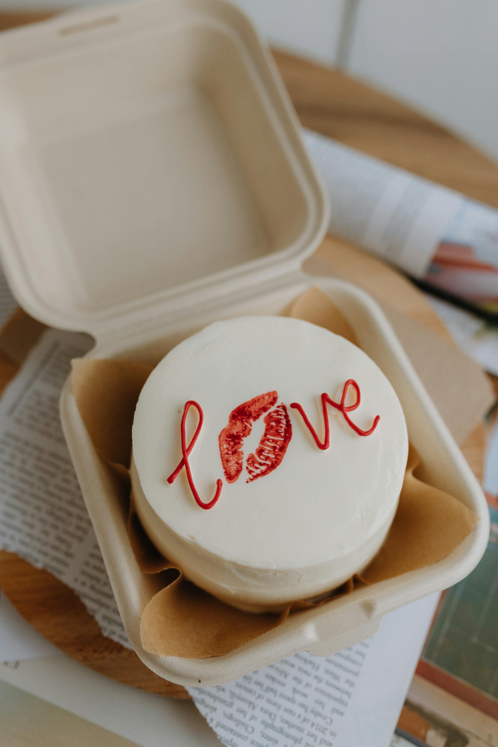 Top view of a white cake with love inscription in an open takeaway box, exuding romance.