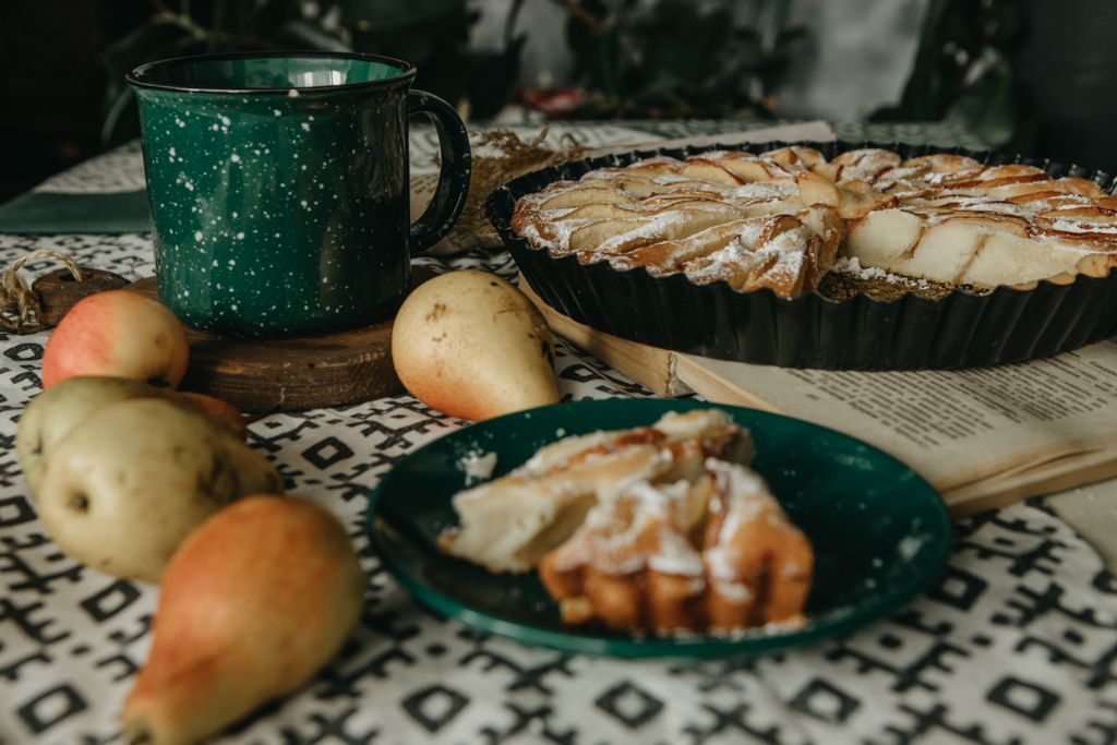 A delicious apple and pear tart with a green mug on a patterned tablecloth.