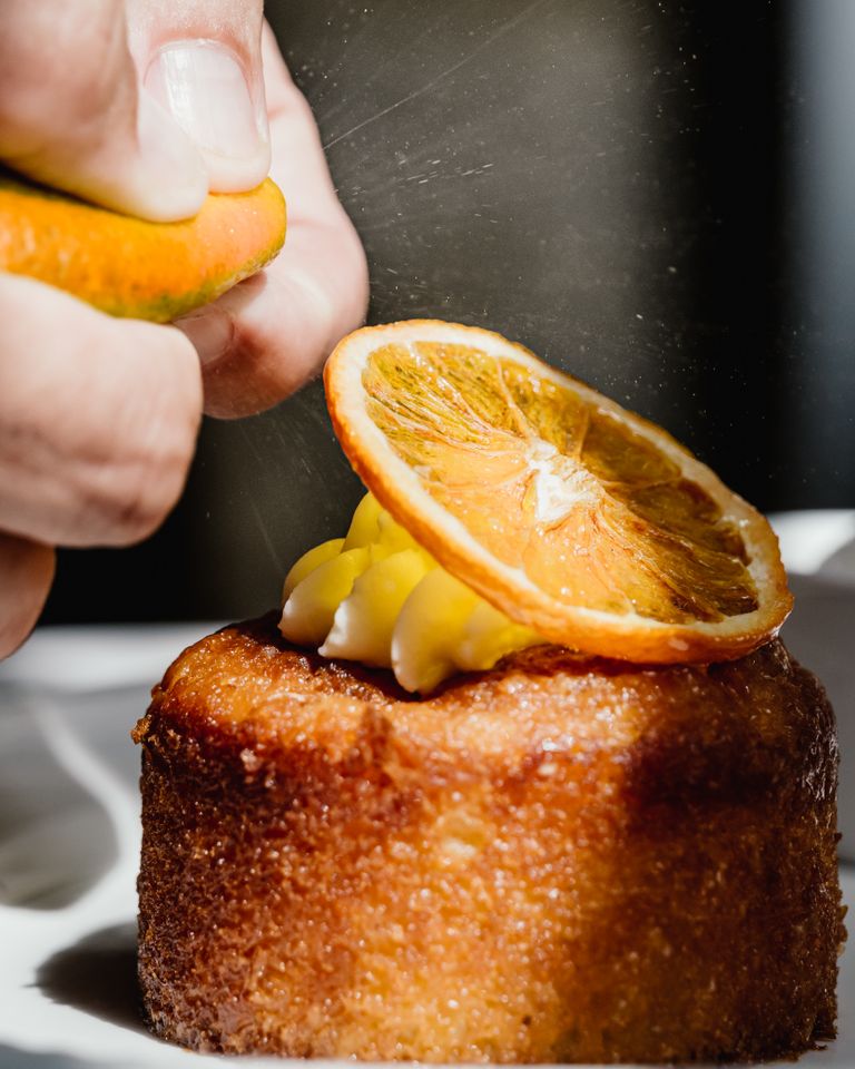 Close-up of a citrus baking cake being drizzled with fresh orange, highlighting vibrant flavors.