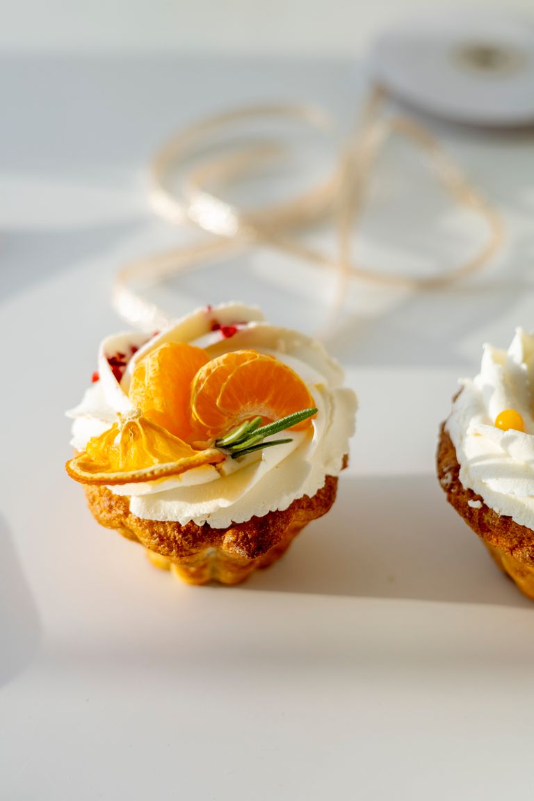 Close-up of a pastry topped with whipped cream, orange slices, and herbs. Perfect for dessert inspiration.