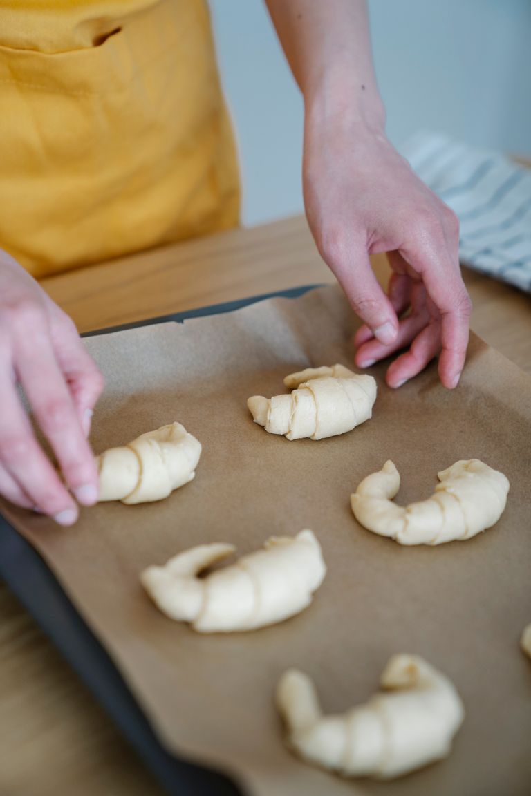 Close-up of hands forming croissants on a baking tray lined with paper.