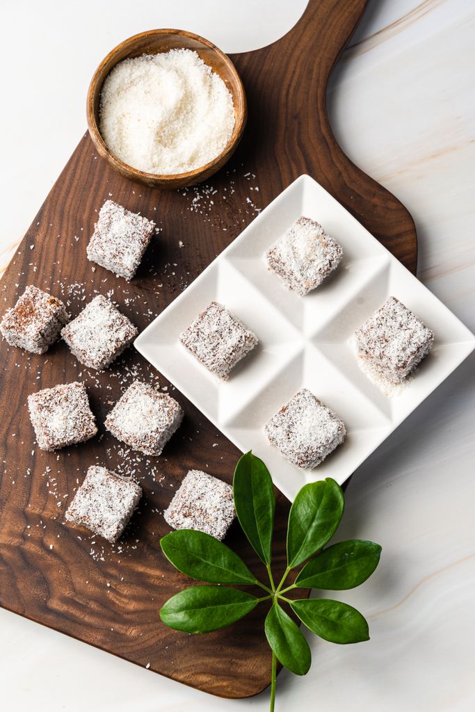 Top-down view of coconut lamingtons on a wooden board with grated coconut - best lamington recipe 