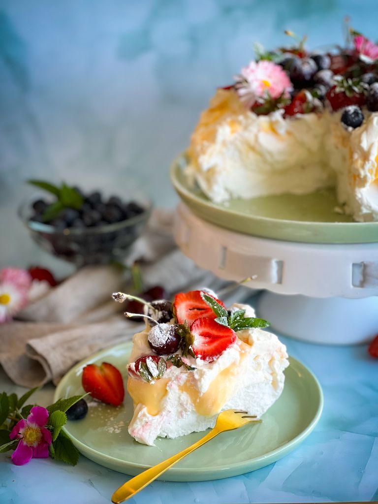 berry pavlova recipe topped with strawberries, blueberries, and cherries on a pastel blue table